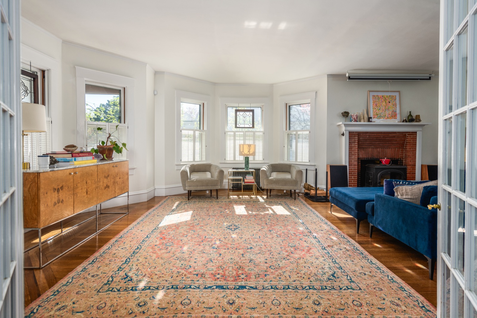 Living room with bay windows, blue velvet sectional, brick fireplace, and Jøtul wood stove.