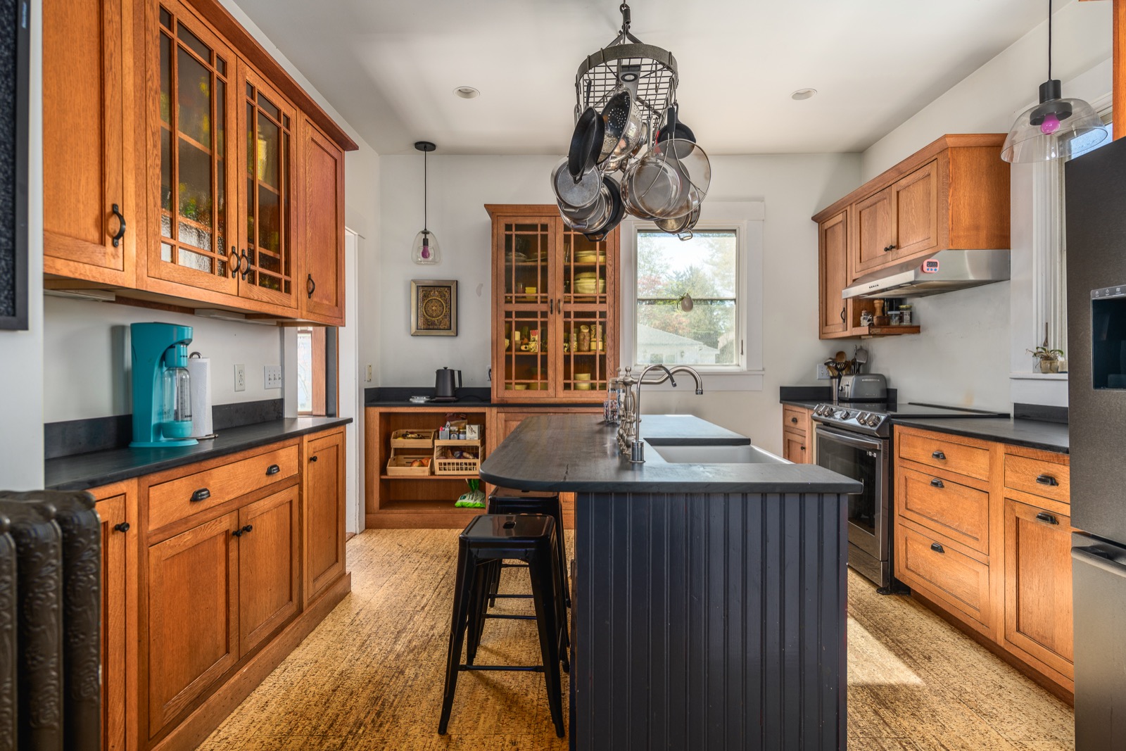 Kitchen with custom wood cabinetry, amber-glass uppers, soapstone island, and hanging pot rack.