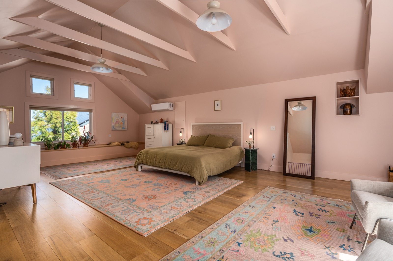 The third-floor primary suite: a wide view showing the full vaulted ceiling, exposed rafters, king bed, dresser, window seat, and depth of the room.
