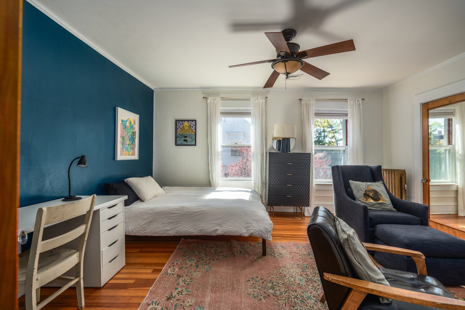 Second bedroom with a queen bed against a teal accent wall and a writing desk under windows.
