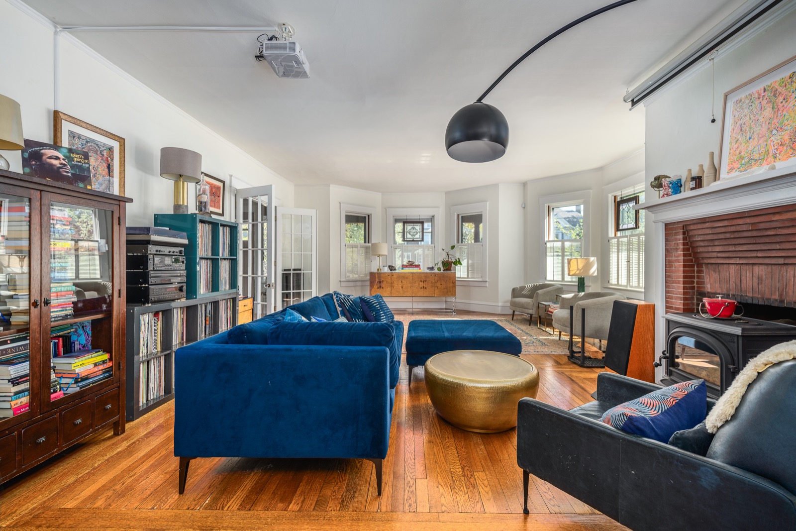Living room from a wider angle, with bookshelves, blue sofa, and bay windows.